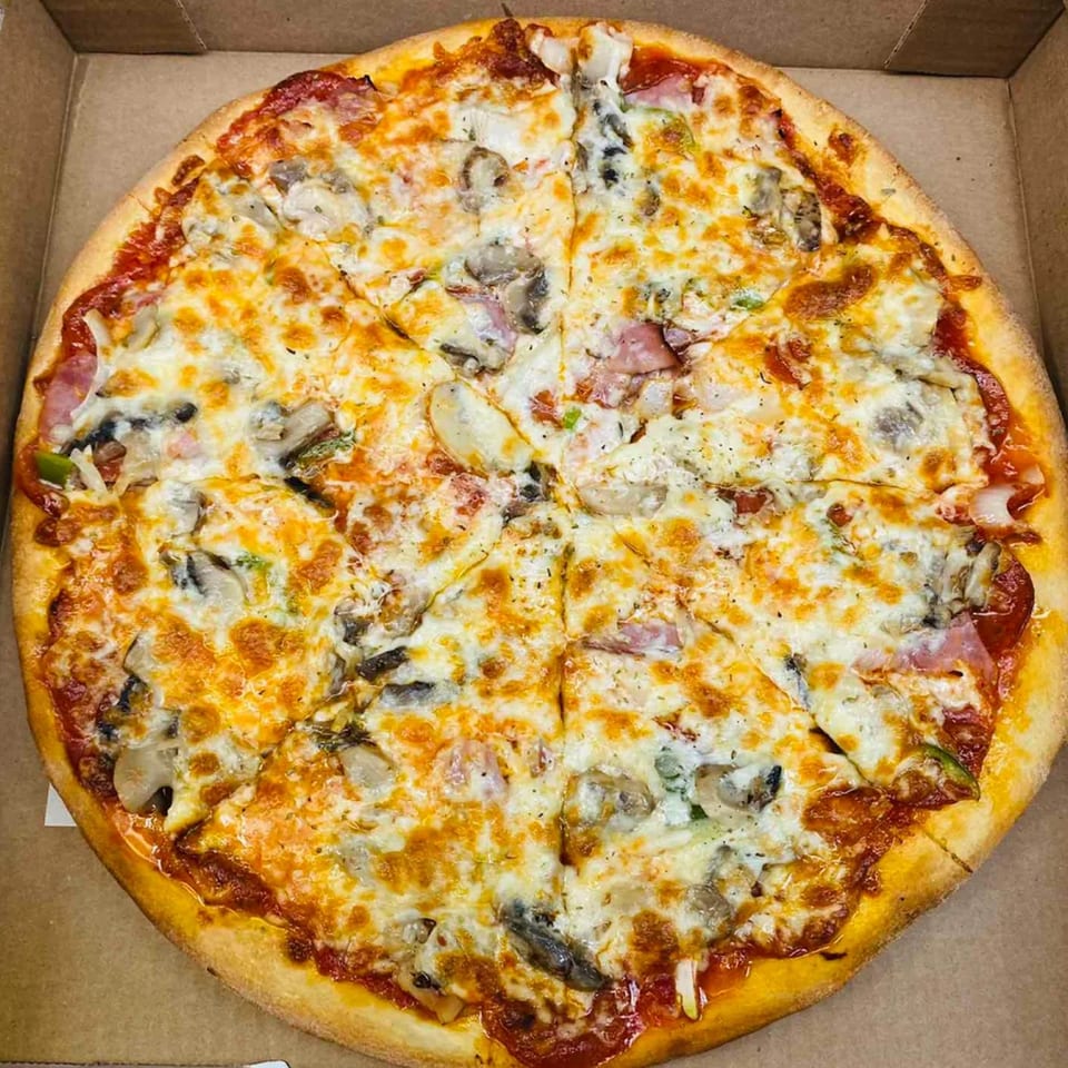 A whole Pascali's Pizza Corner pizza, topped with melted cheese, mushrooms, ham, and green peppers, in a cardboard box.