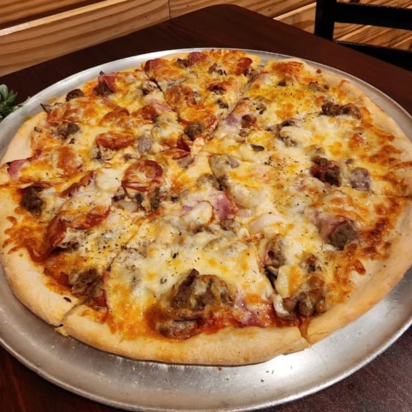 A large, sliced Pascali's Pizza Corner meat lover's pizza with pepperoni, sausage, and ham.