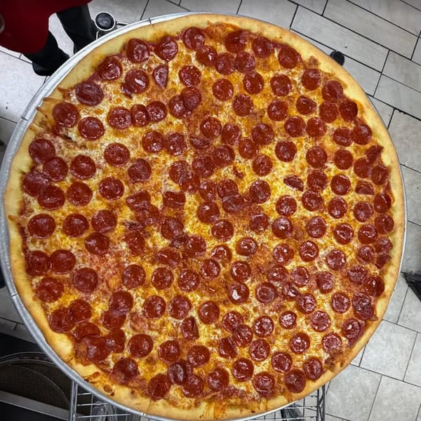 A large, round Pascali's Pizza Corner pepperoni pizza with melted cheese on a metal tray.
