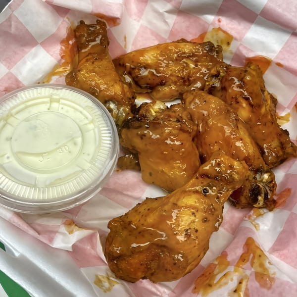 Pascali's Pizza Corner's saucy chicken wings with a side of ranch dressing in a takeout container.
